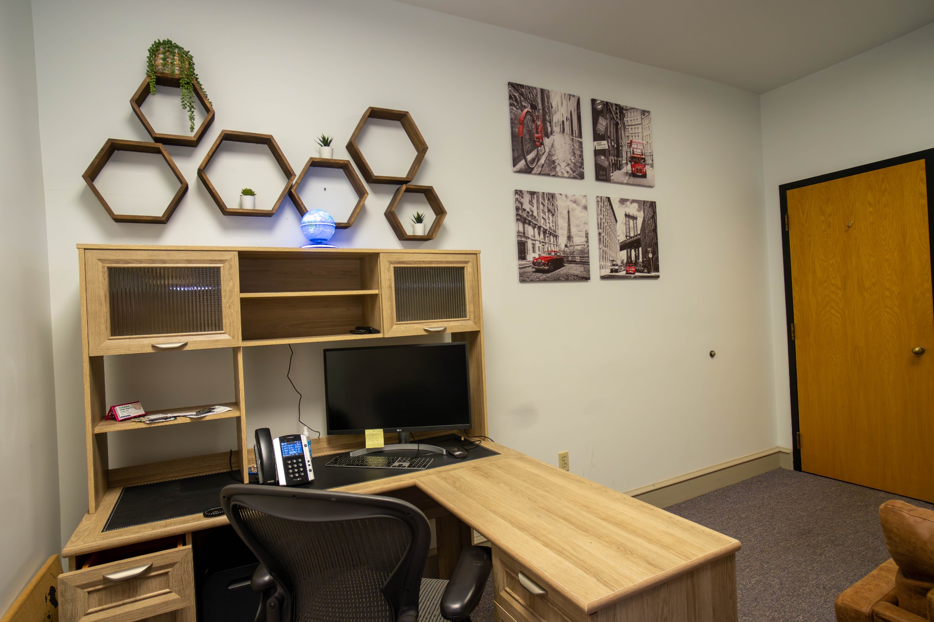 Private office with hexagonal wall shelves and travel-themed canvas art