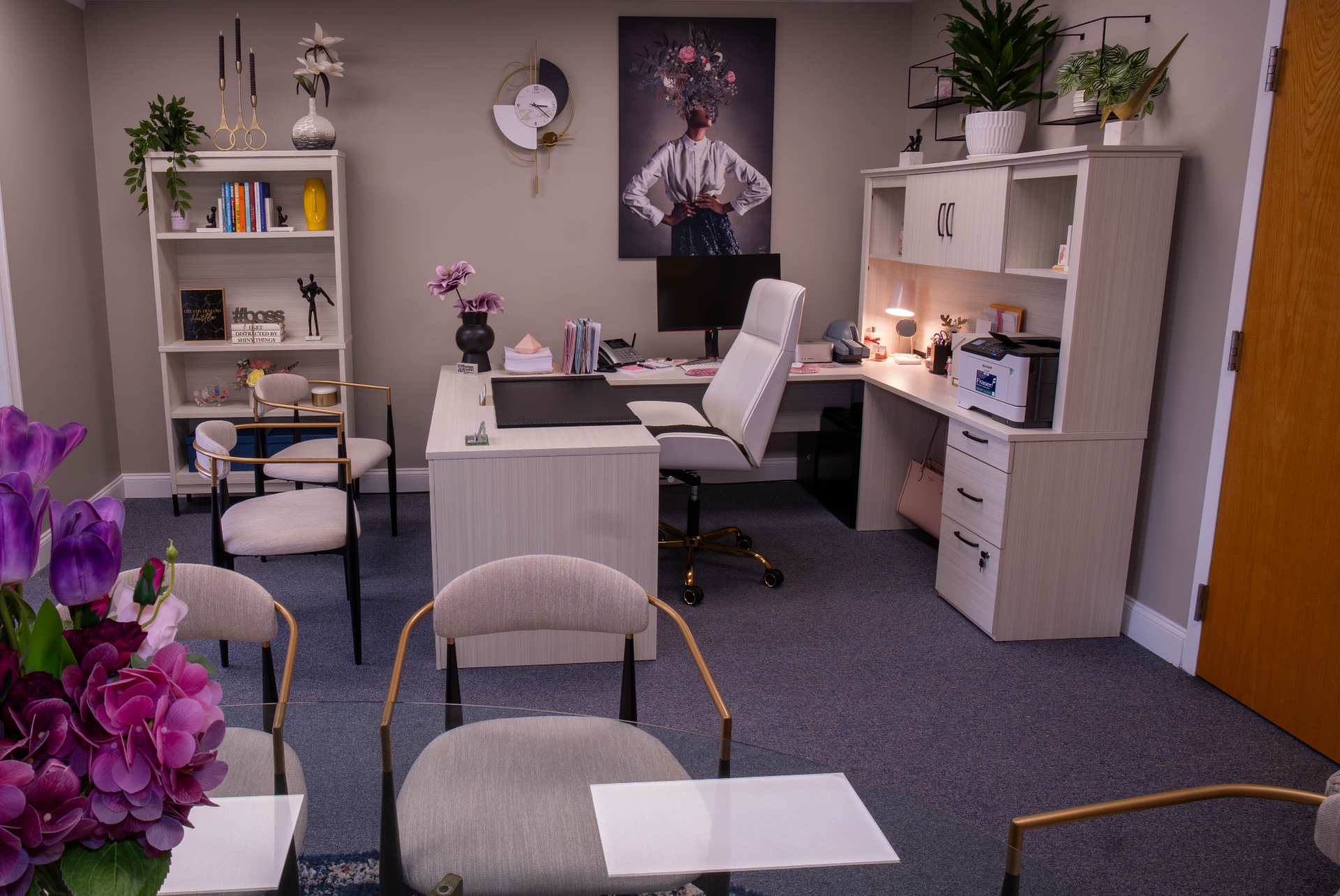 Executive office with white desk, gold accents, and floral portrait art