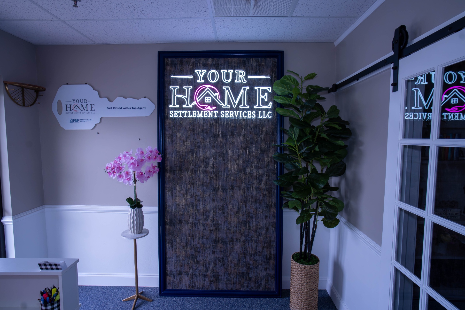 Neon-lit Your Home Settlement Services signage with key plaque and styled entry
