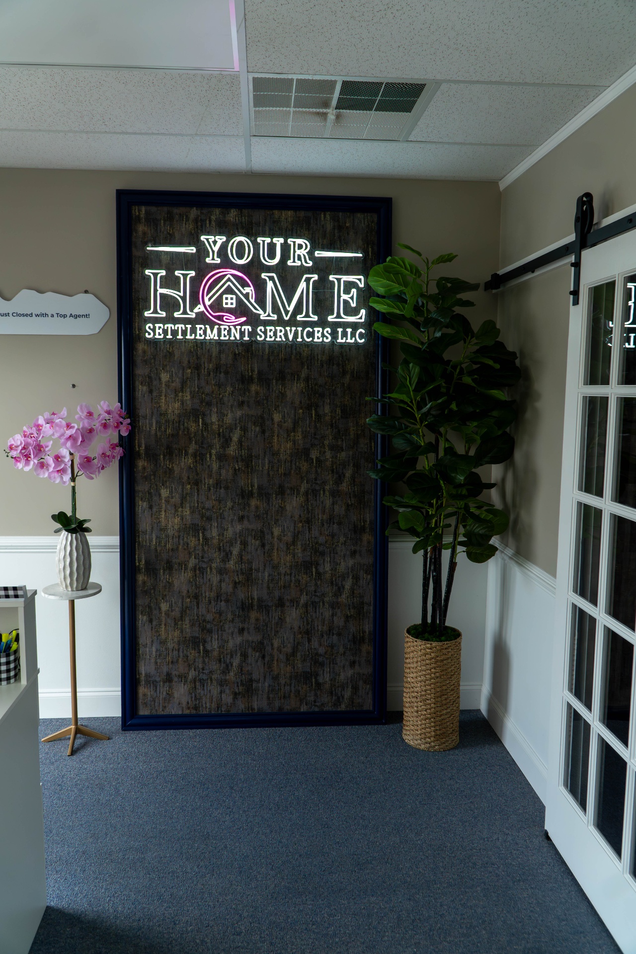 Vertical view of the neon settlement services feature wall with orchid and fiddle leaf fig