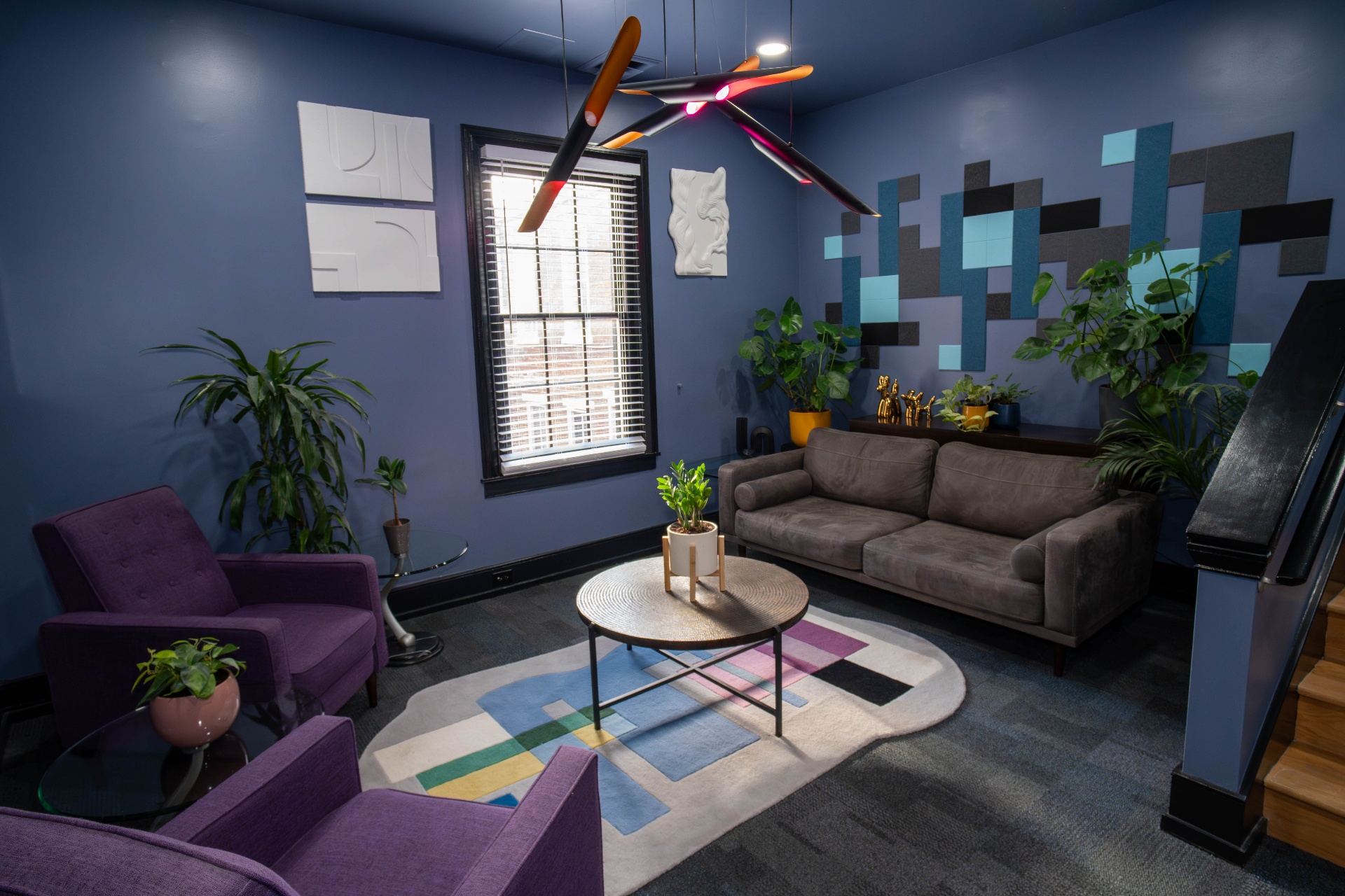 Periwinkle lounge with purple chairs, sculptural pendant, and acoustic tile wall art